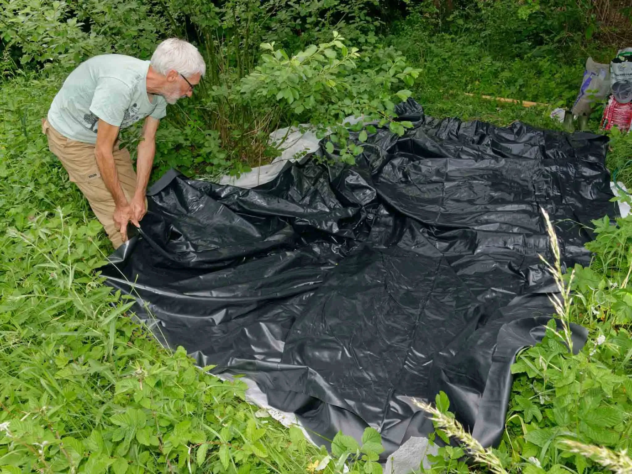 A man fitting his pond liner to his large pond.
