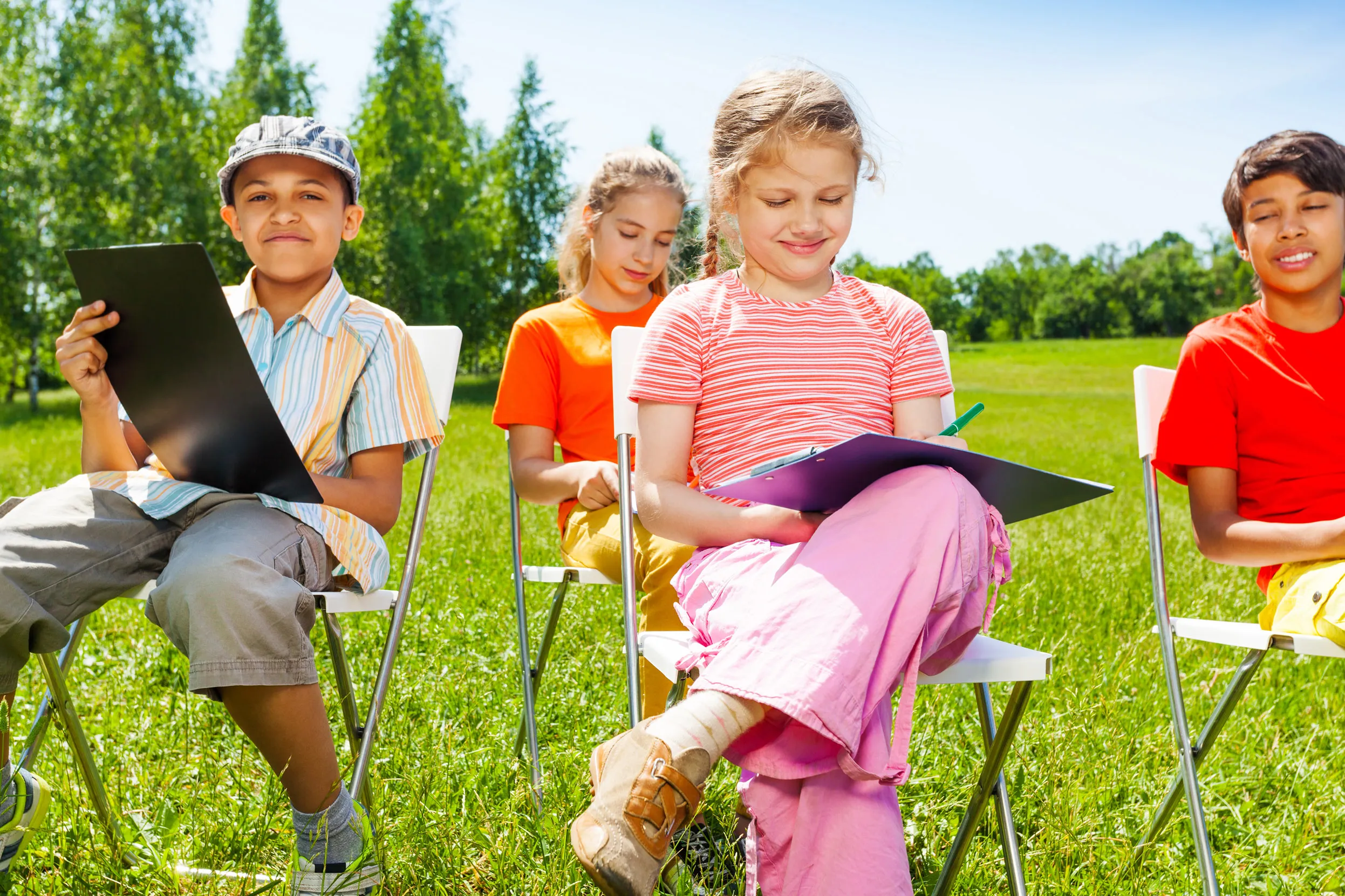 A group of four children sat outside on chairs making notes on clipboards.