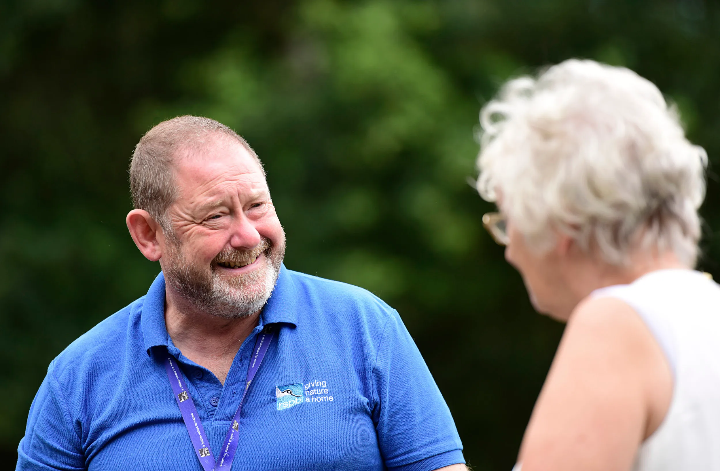 A member of RSPB staff talking to a member of the public with trees in the background.