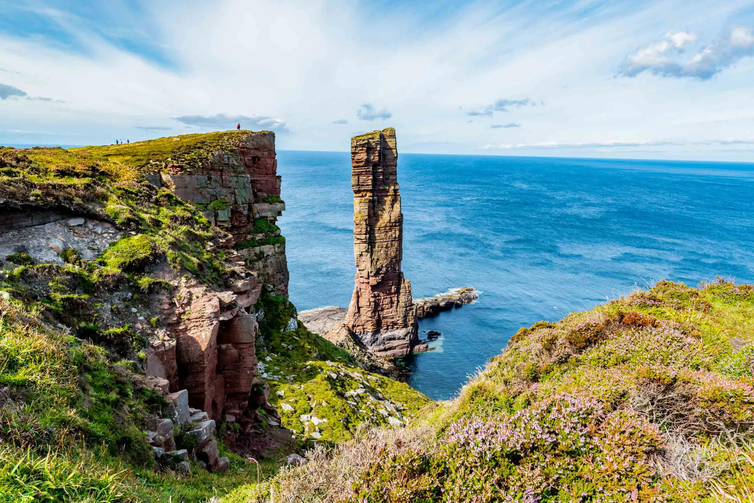 As we stand on the grassy cliffs at Hoy, The Old Man sea stack formation stands tall in the bright blue waters.