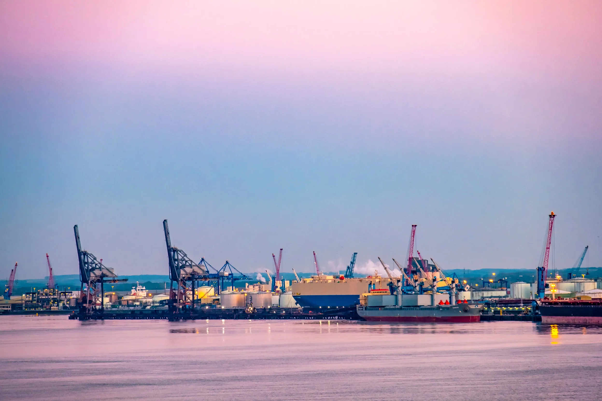 A large dock with a skyline scattered with cranes and lights.