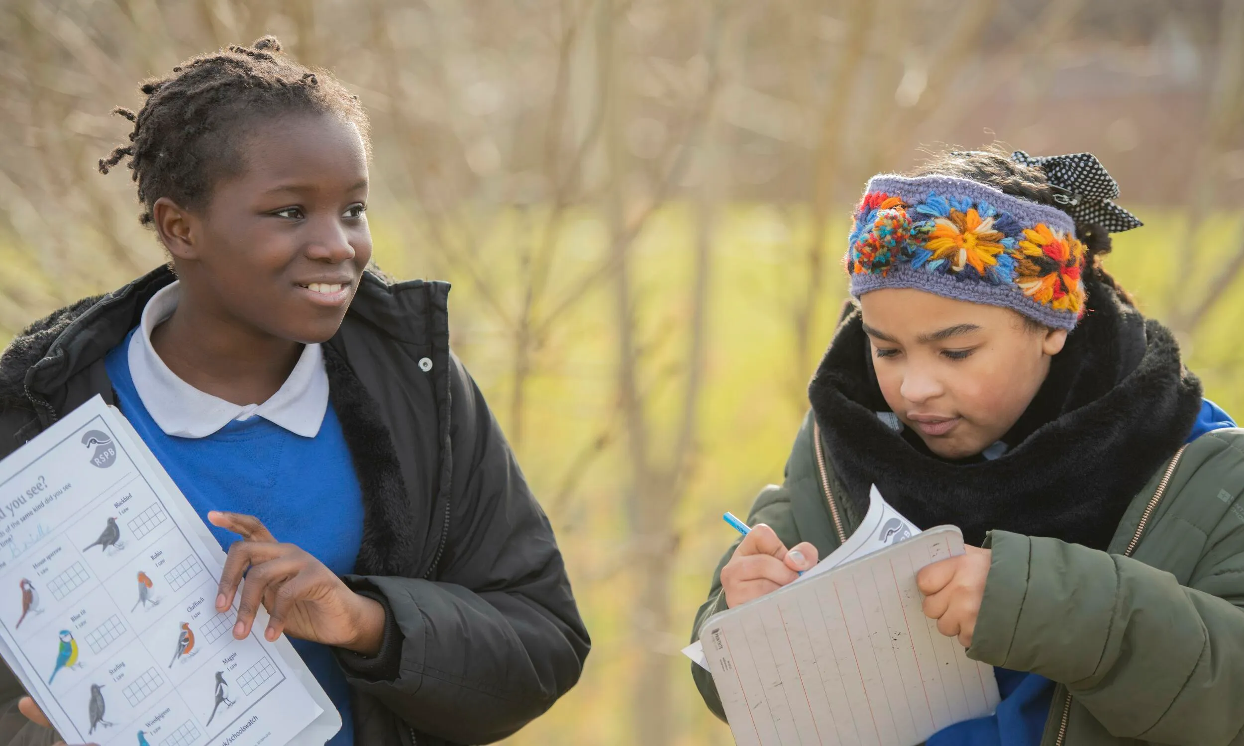 Children in school uniforms and winter jackets, taking part in Big Schools Birdwatch, recording their results on paper 