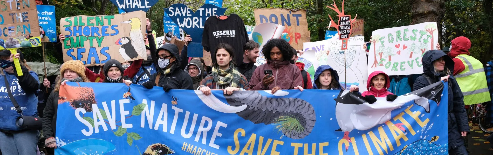 A group of people marching with handmade signs and a large banner which reads, 'Save nature, save the climate'.