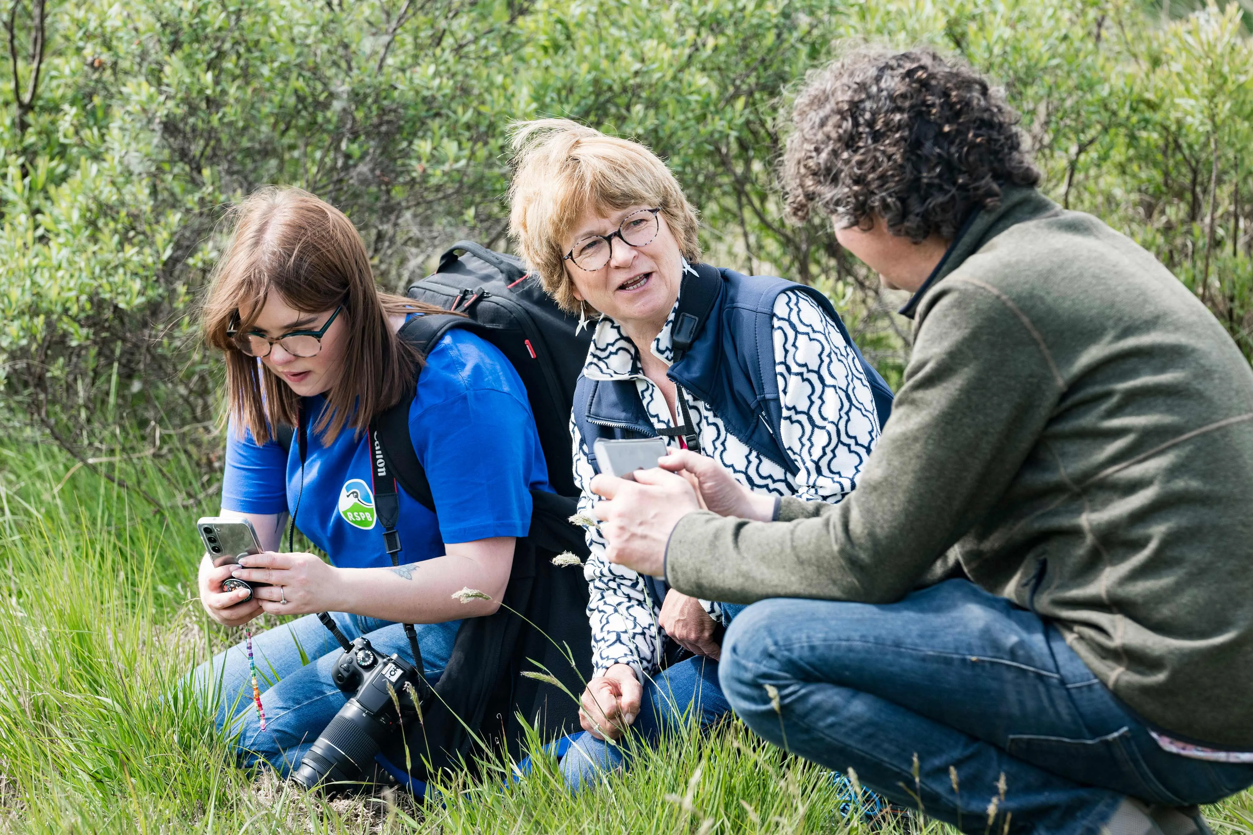 Three RSPB volunteers chatting together whilst sitting in grass.