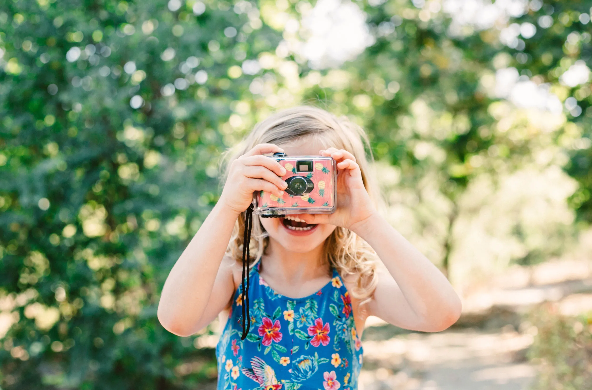 A small child stood on a path in a woodland, looking through a camera to take a picture.