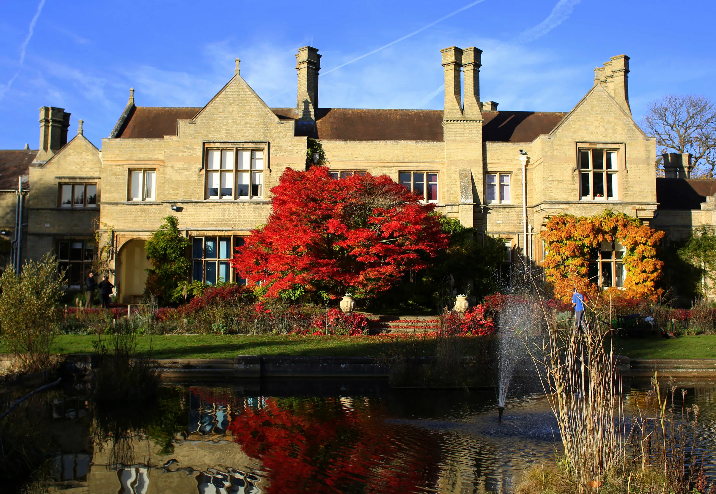 A view of The Lodge from the garden pond. Surrounded by autumnal trees.