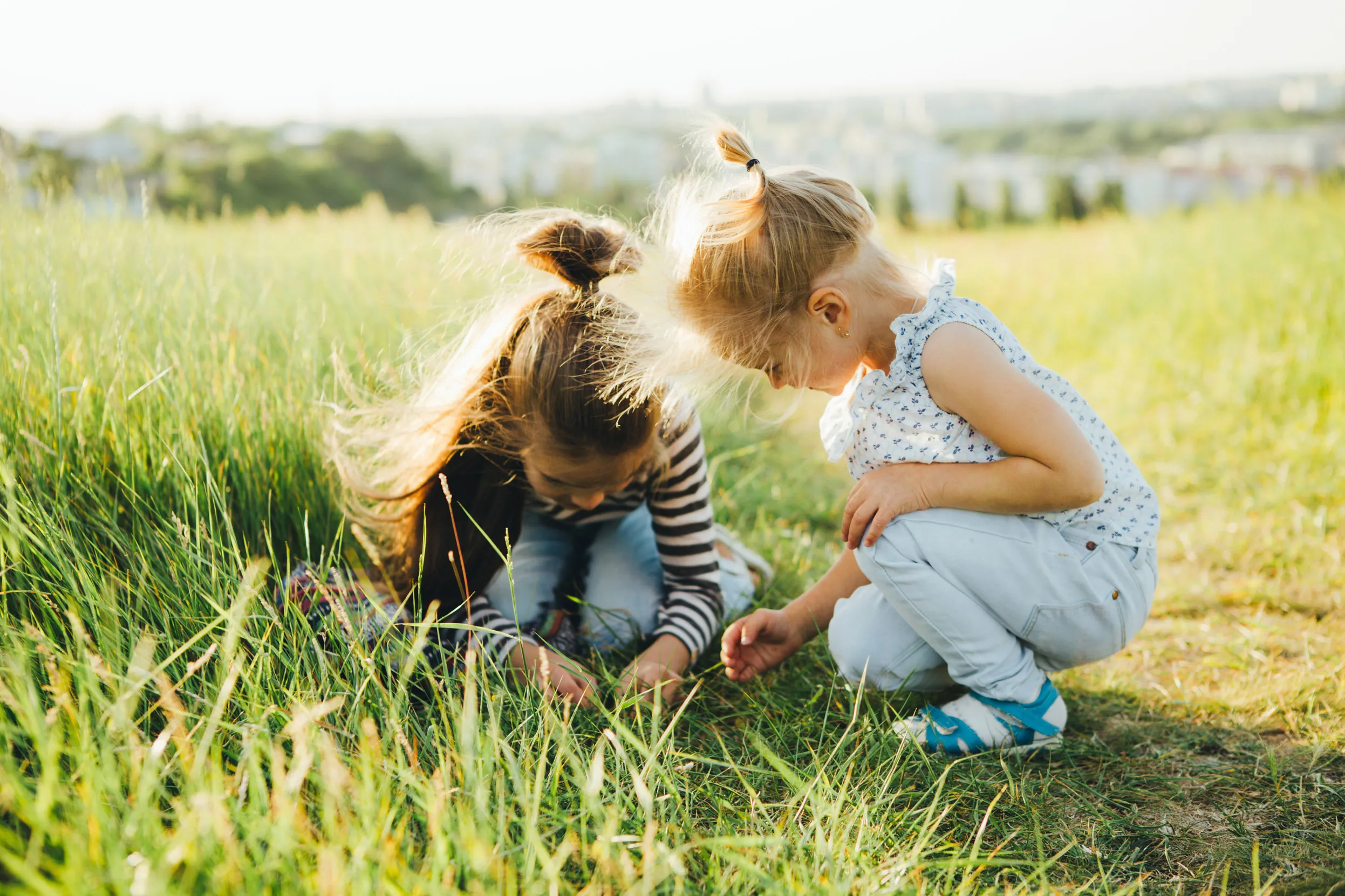 Two children crouched on the edge of a field path, investigating what they can find in the longer grasses.