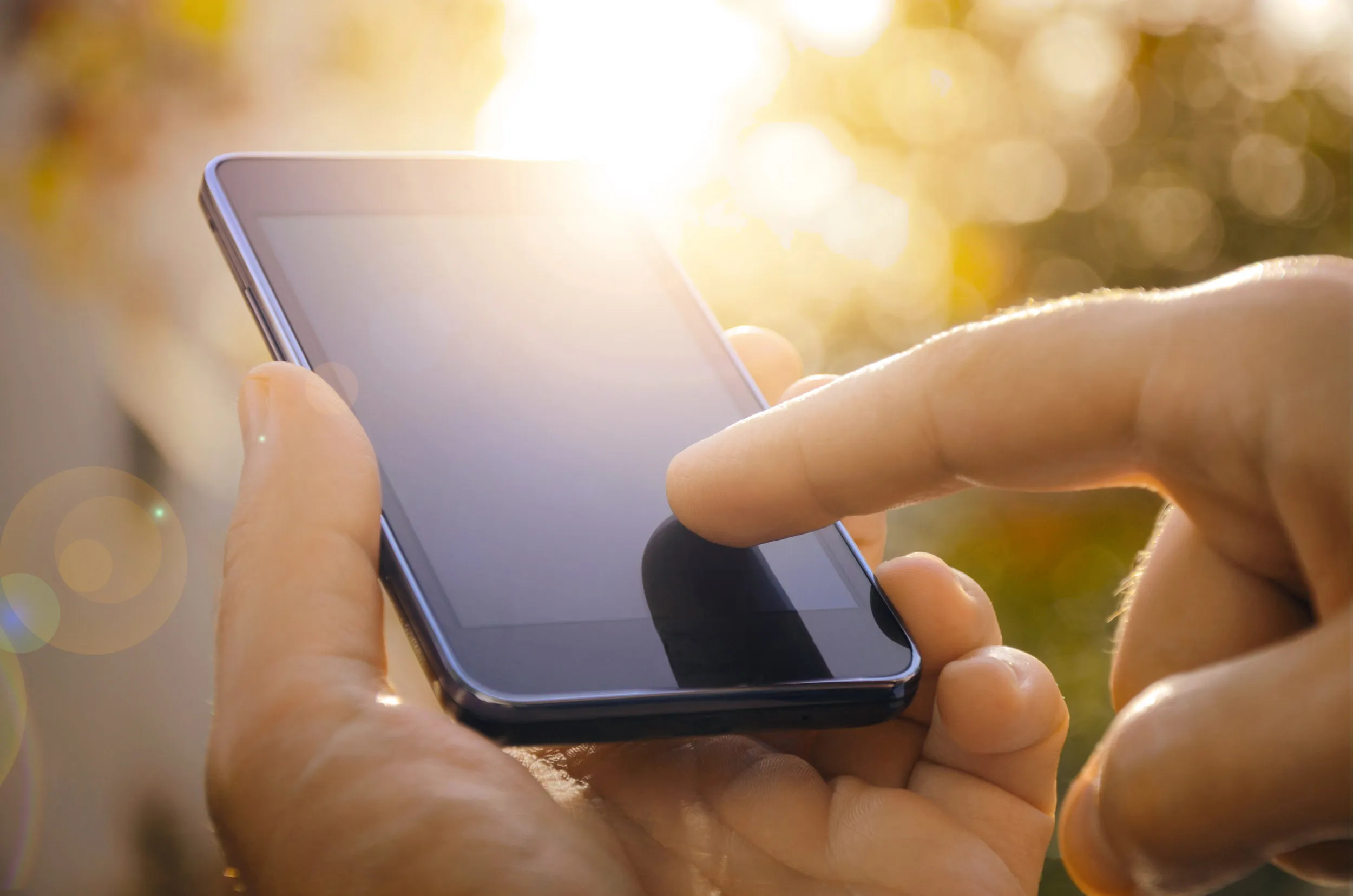 A person touching their smartphone screen, with a low sun setting behind.