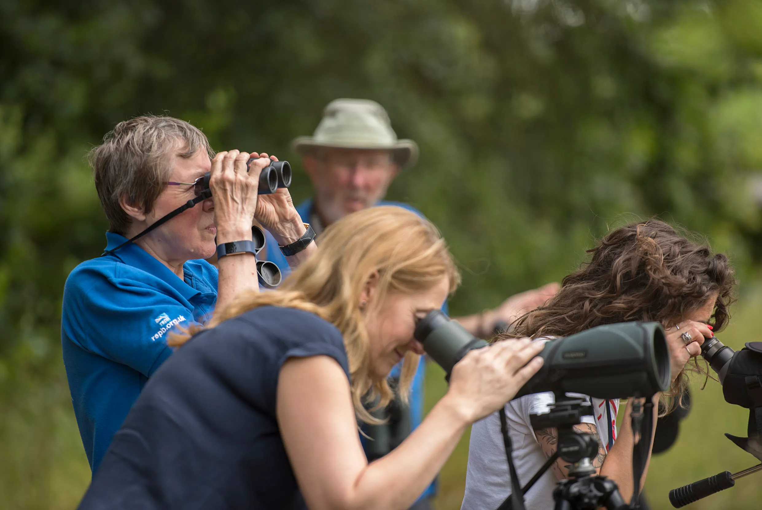 A group of people birdwatching through a telescope with an RSPB staff member using binoculars. 