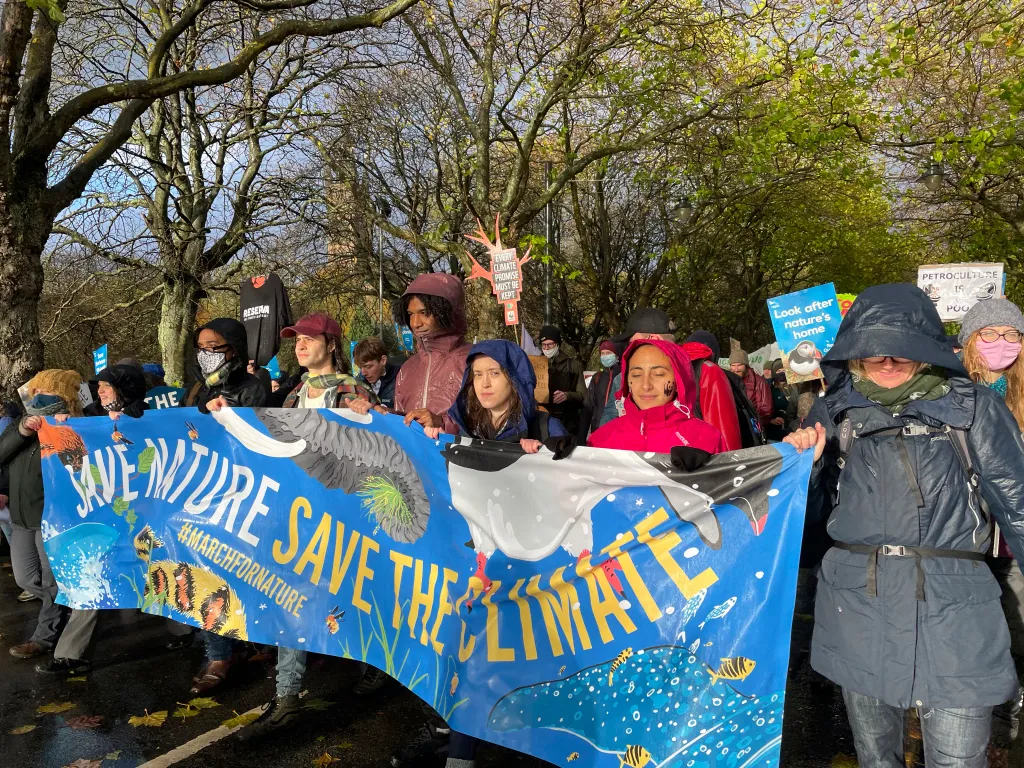 A group of people marching with a large banner which reads "Save Nature, Save the Climate".