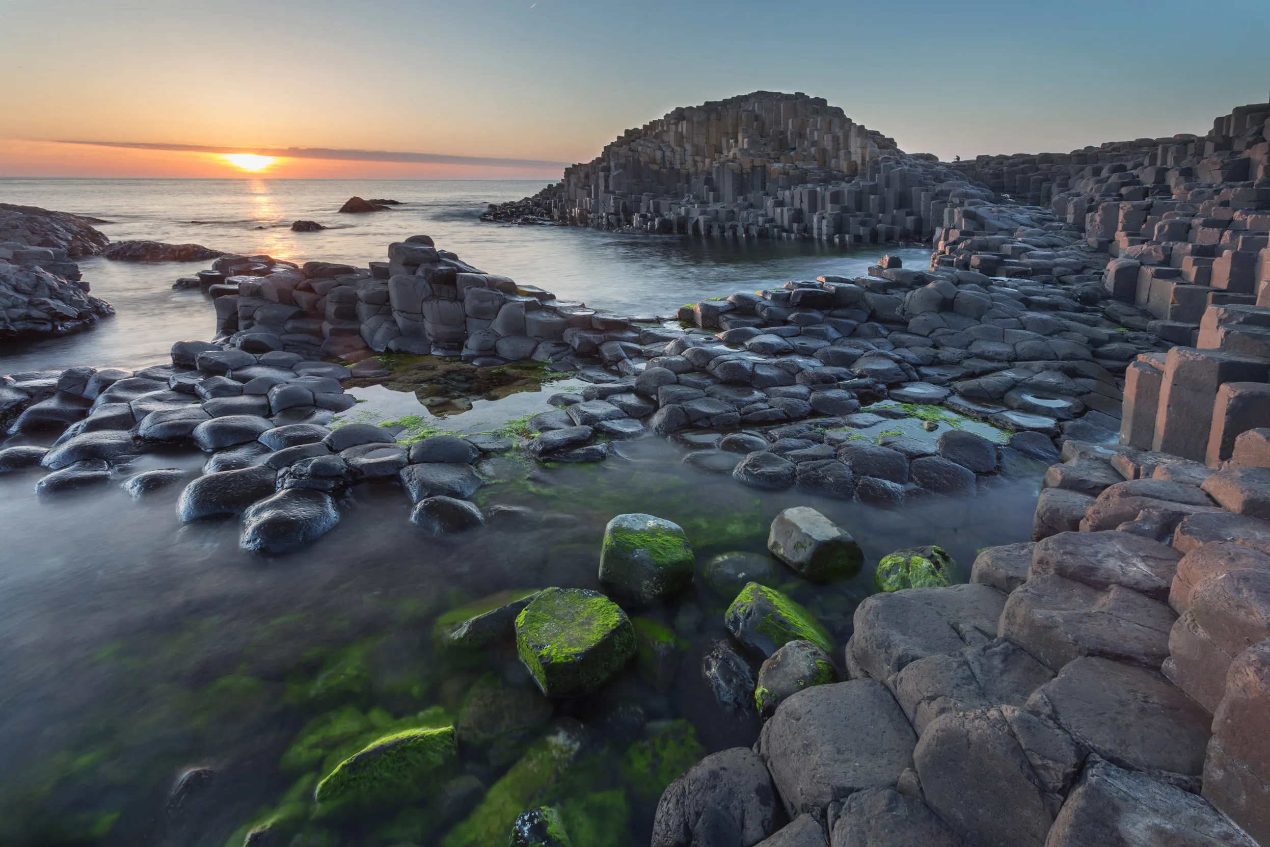 Sun sets over Giant's Causeway filling the sky with orange tones.