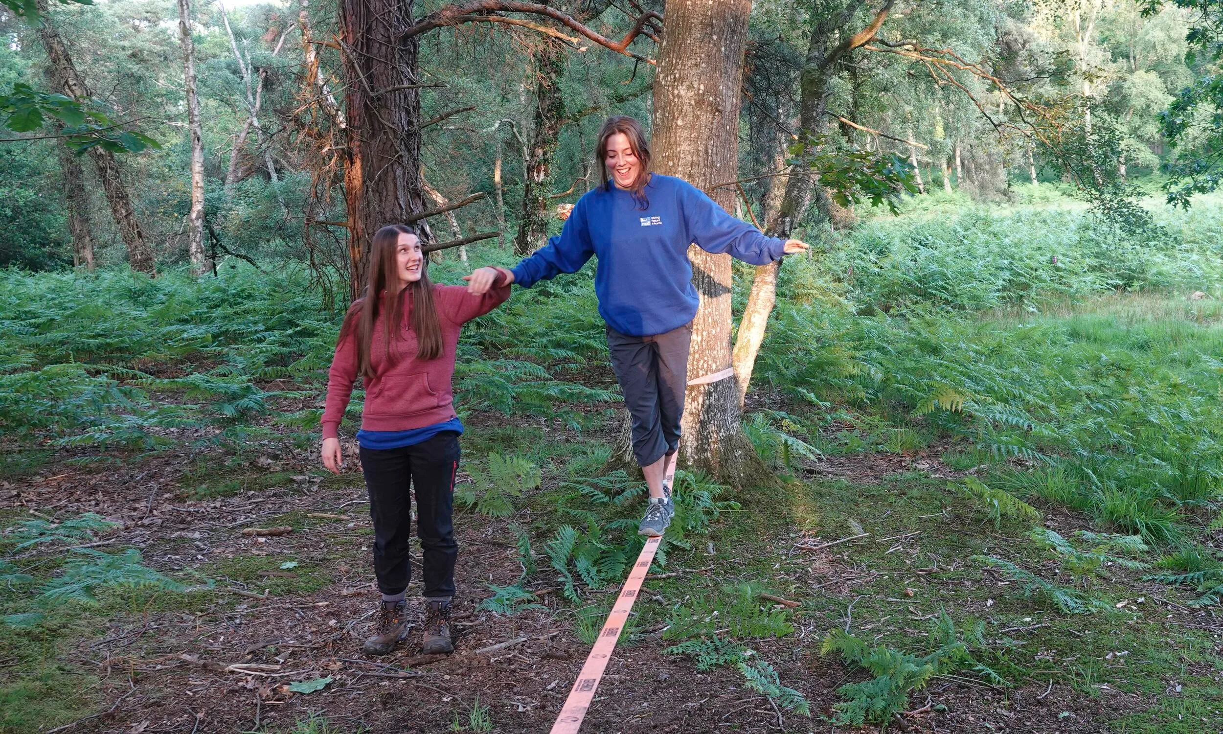 A person having a go at slack lining, in a forest setting
