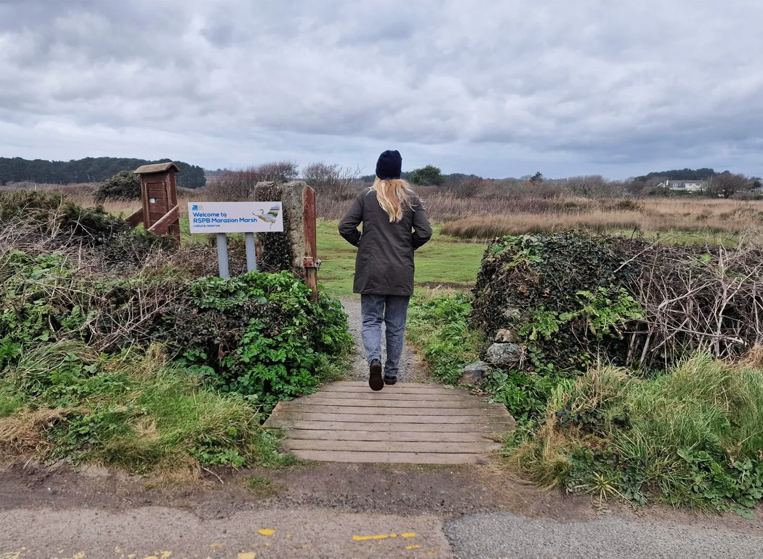 A person in a green coat walking through the entrance at Marazion Marsh in West Cornwall, UK