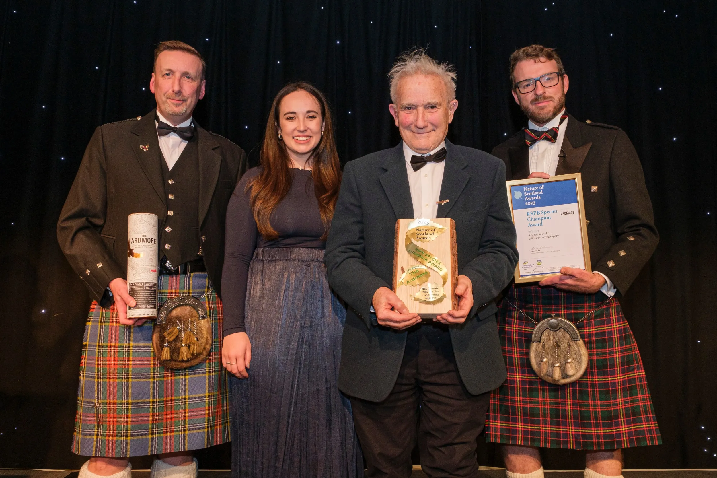 4 people, smiling towards the camera, one holds a trophy, one a certificate, and the other a bottle of The Ardmore whisky