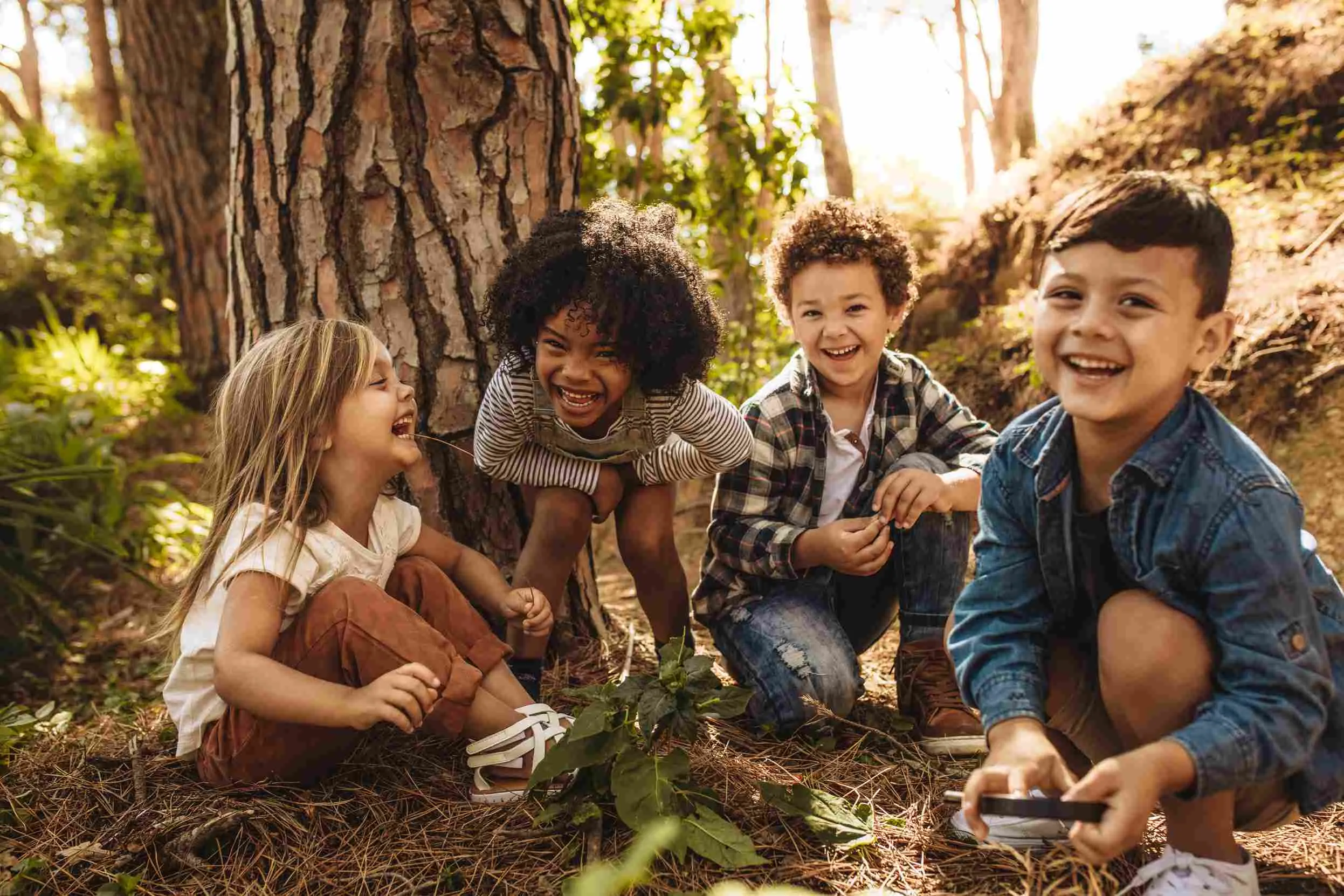 Four children crouched on the forest floor, smiling and laughing.