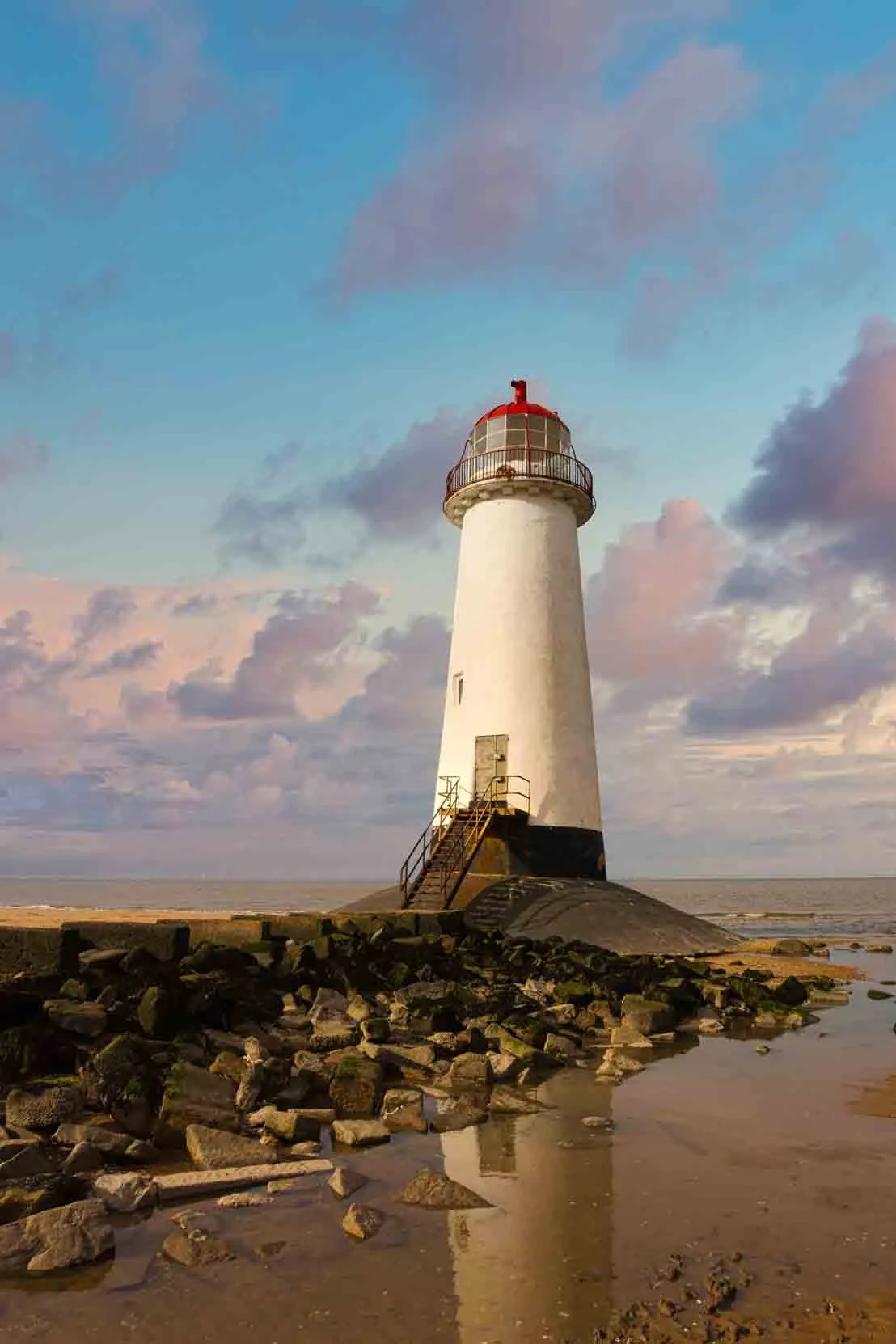 Point of Ayr Lighthouse stood tall in surrounded by shallow waters against and blue sky with pink clouds.
