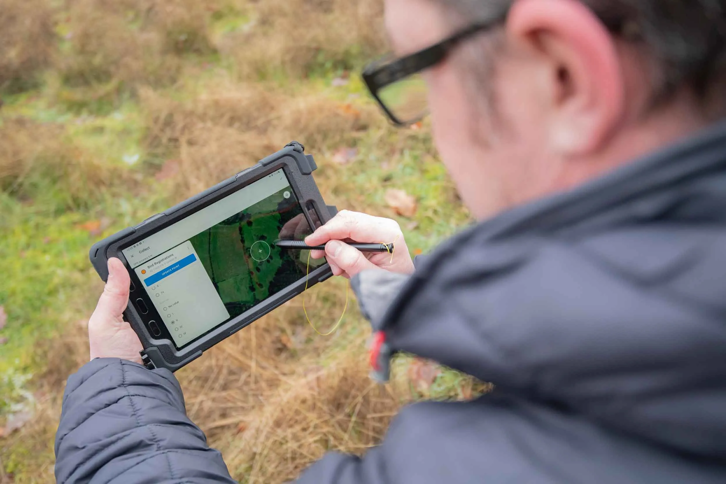 A view over the shoulder of a man using scientist mapping technology in a field. 