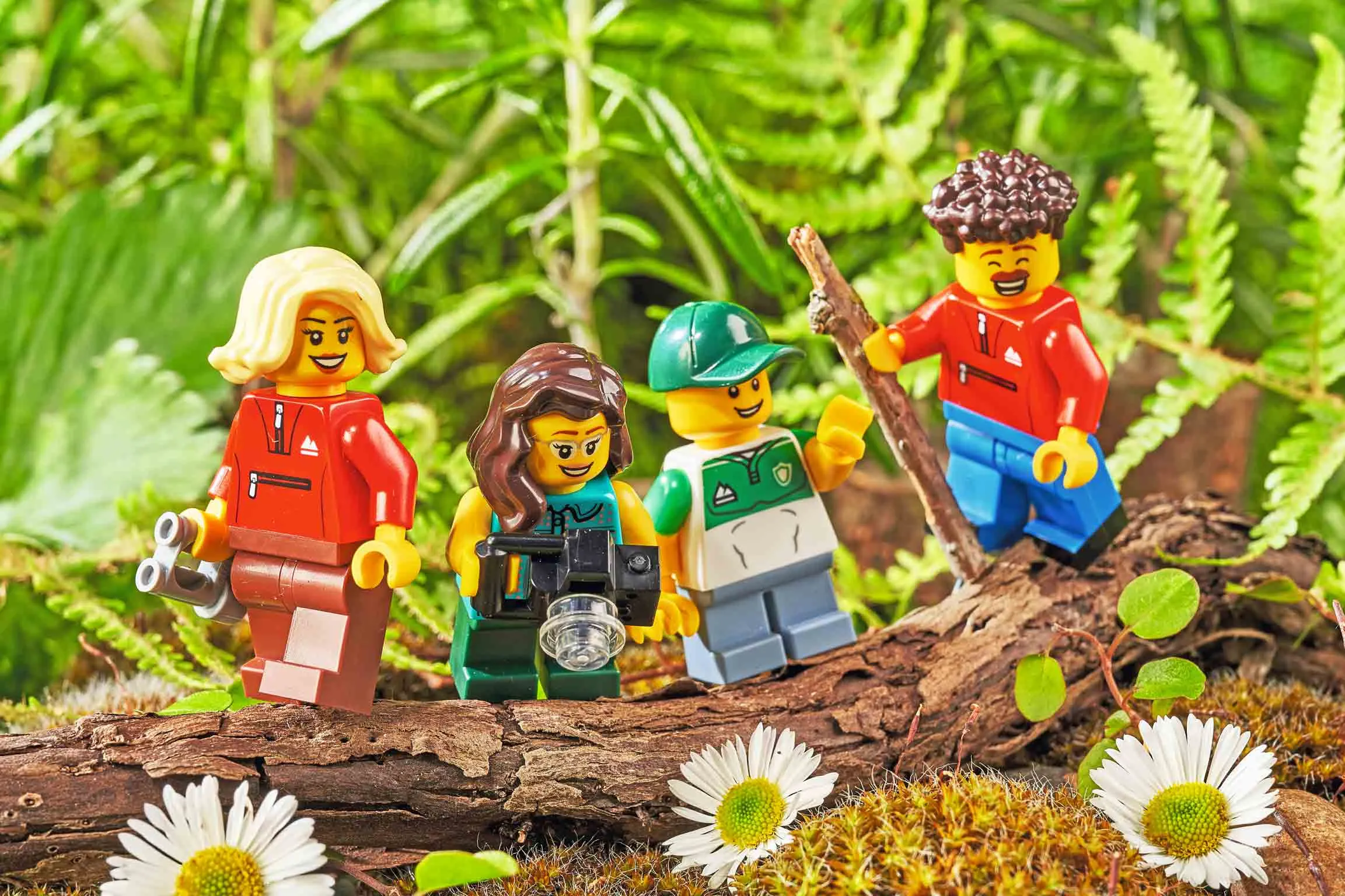 Four LEGO® figures, dressed in outdoor adventure gear, placed on a log and surrounded by ferns and daisies.