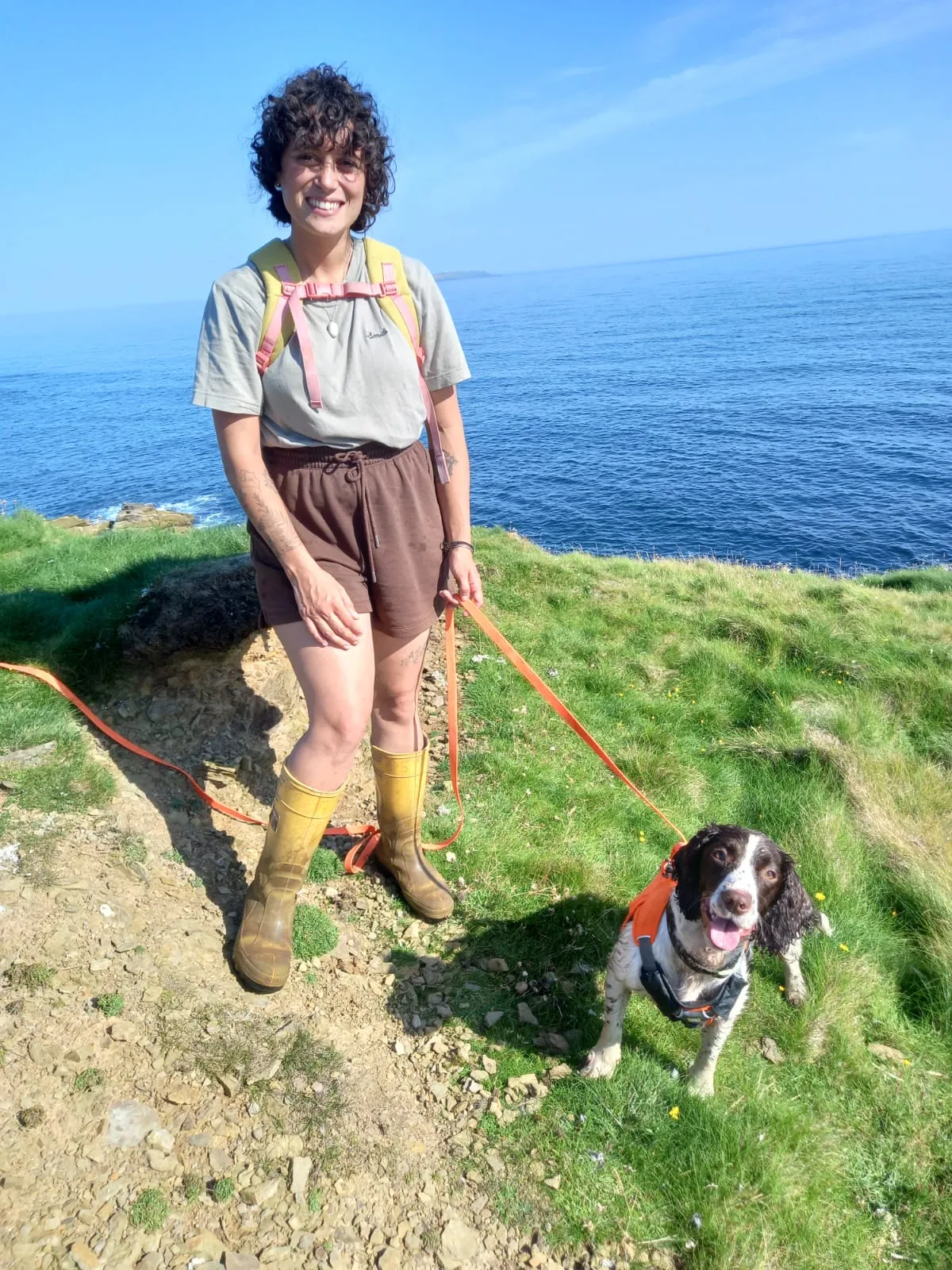 A woman and her Springer-spaniel sniffer dog stood atop a cliff next to the sea.