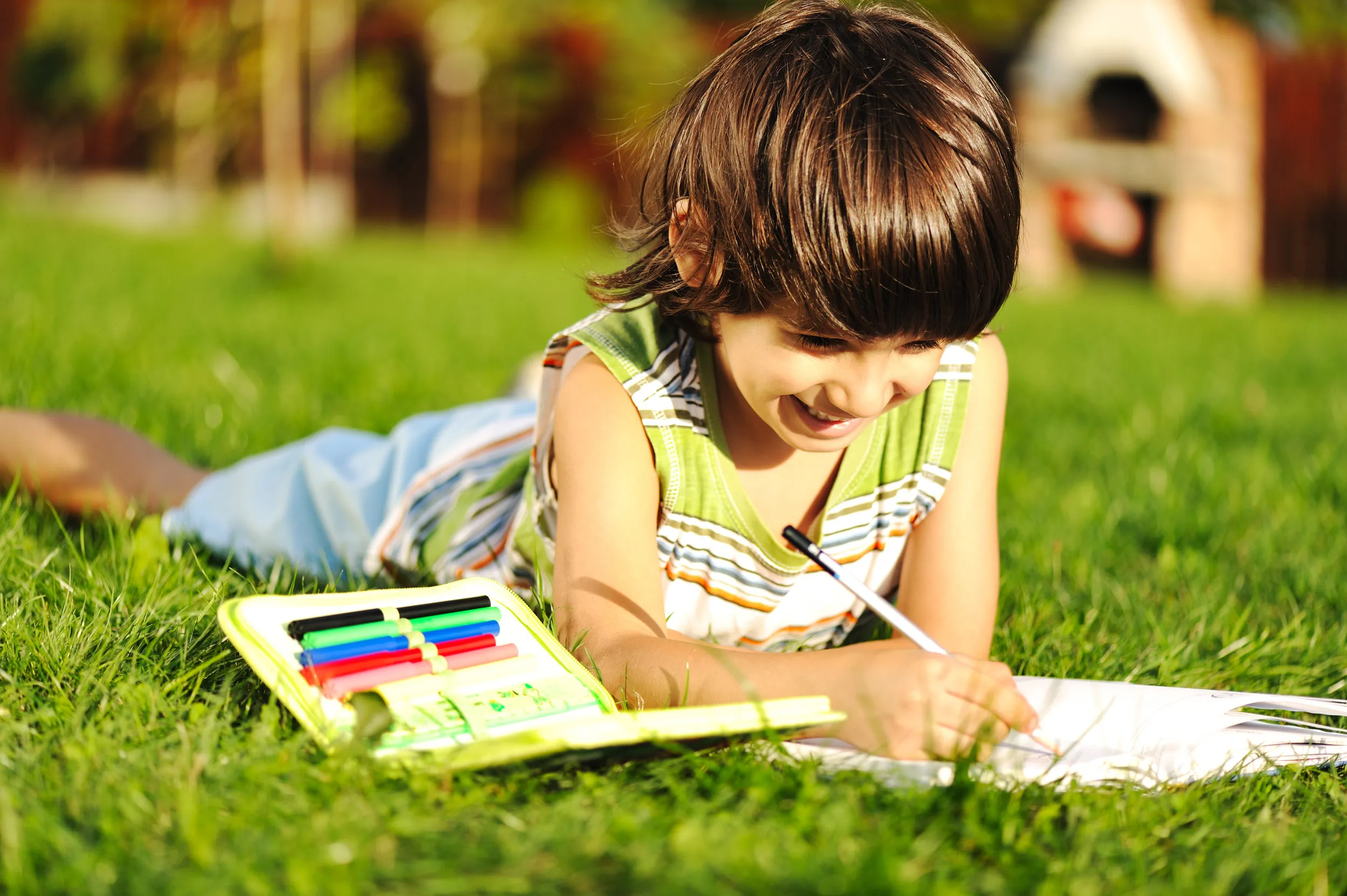 A child laying on a bed of grass with a pencil case and book.