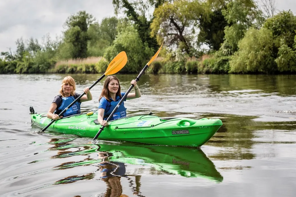 Two people in smiling RSPB branded life jackets, sitting in a bright green two-person kayak.