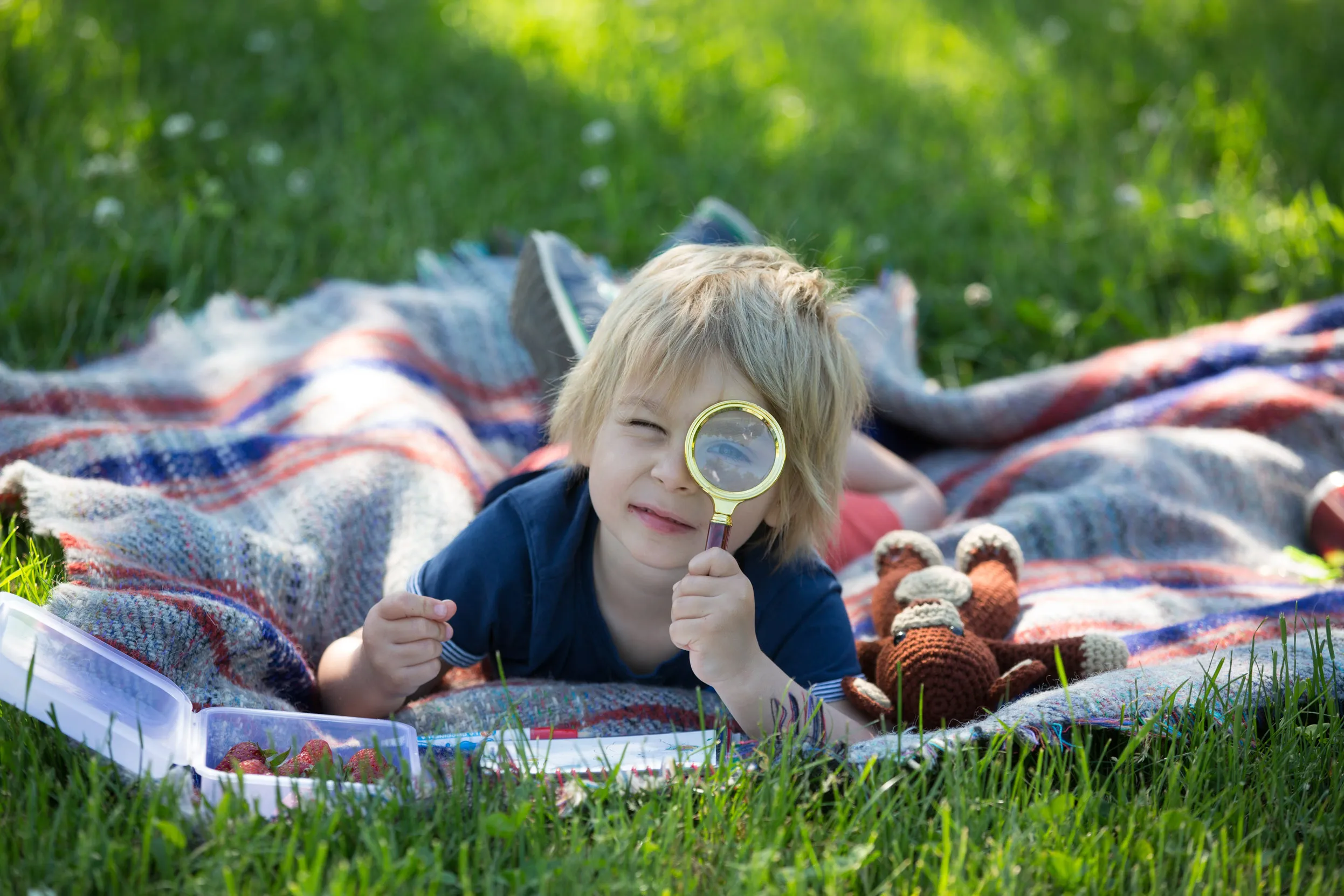 A child laying outside on a blanket looking through a magnifying glass.