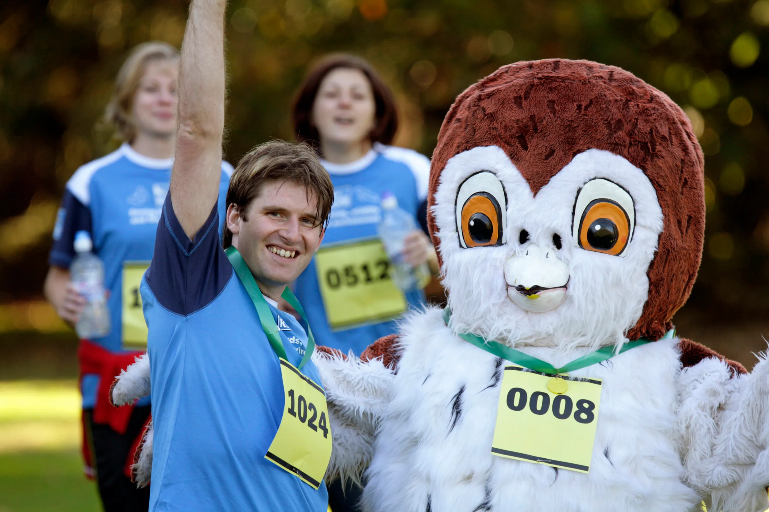 A group of people in blue t-shirts fundraising, doing a fun run with someone dressed as an owl.