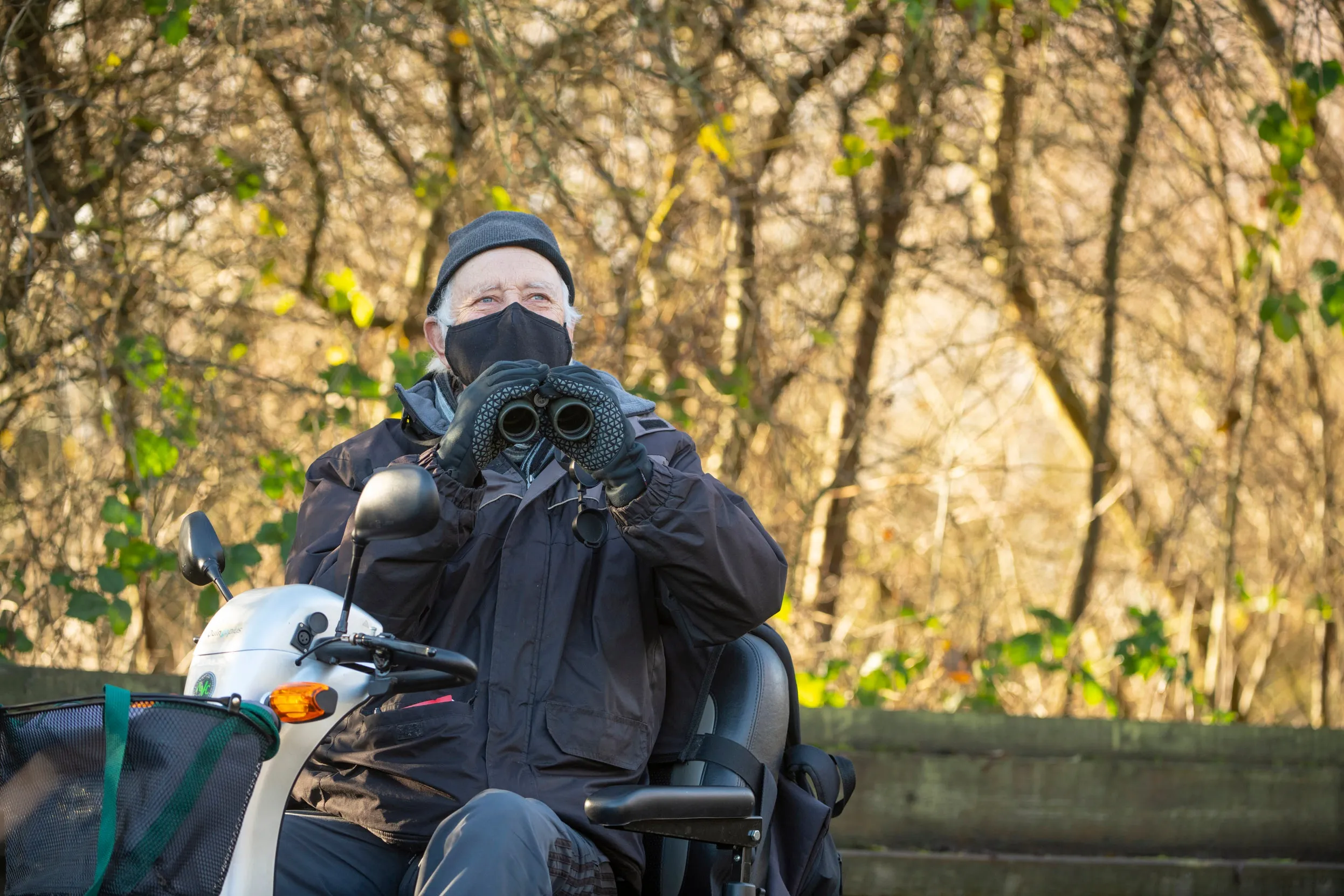 A man wearing a mask on a mobility scooter holding binoculars at RSPB Rye Meads.