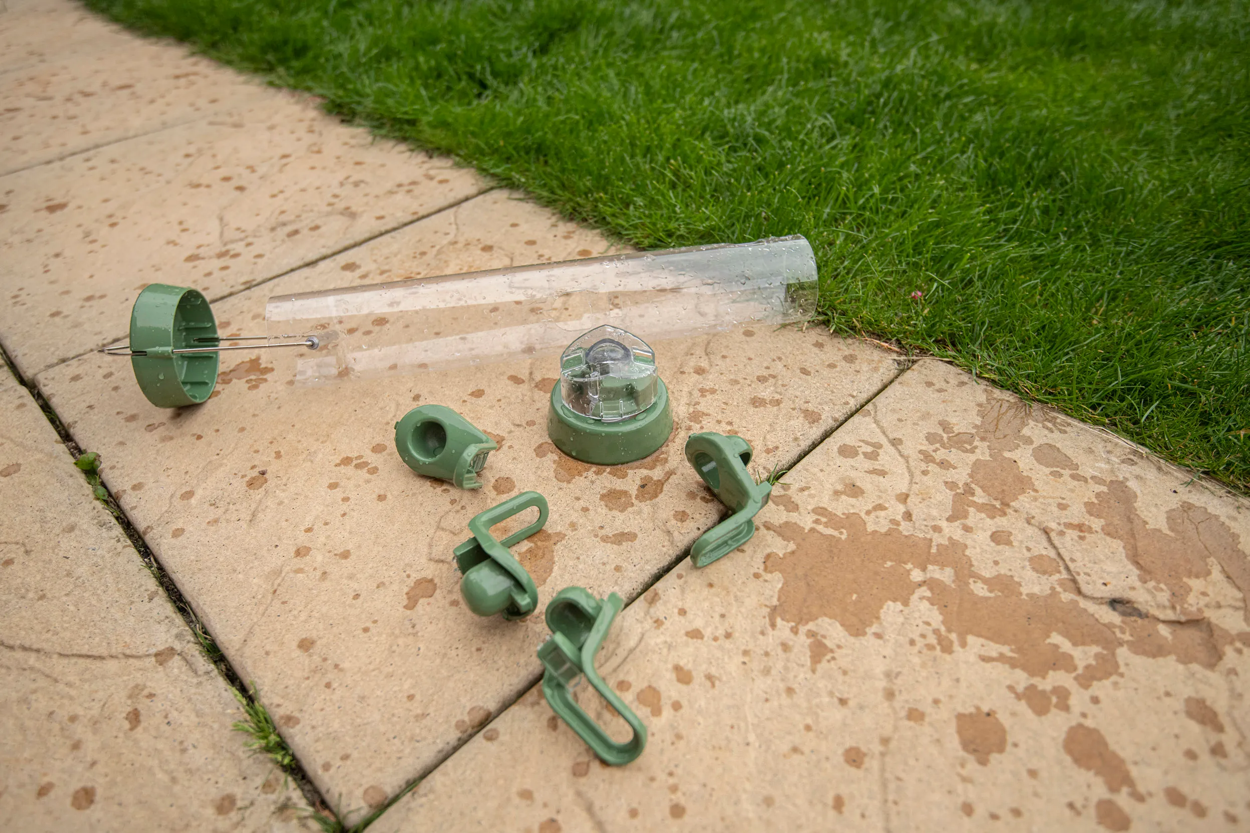 All the parts of a domestic bird feeder laid over concrete garden slabs, next to the grass, to dry.