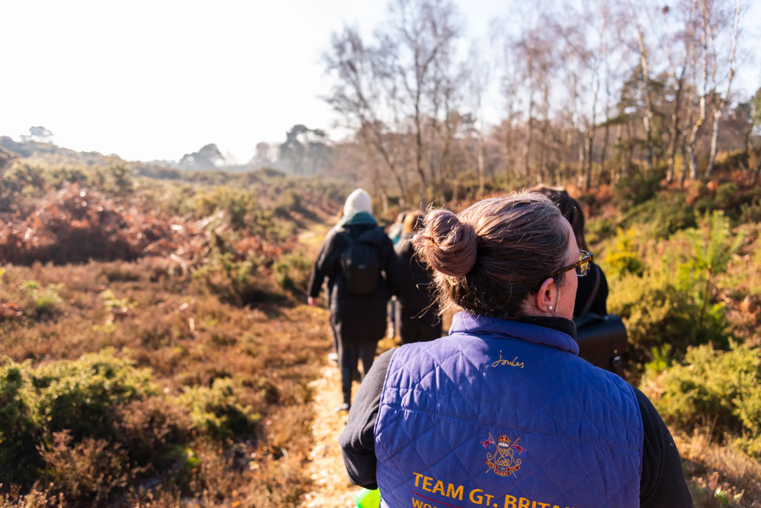 A line of people walking down a path with shrubbery either side at RSPB Arne during winter.