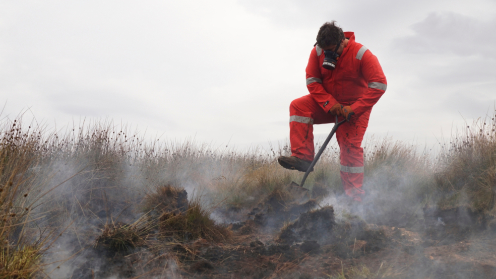 A working tackling the remains of a peatland fire.